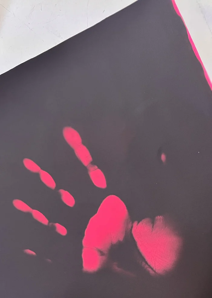 A bright pink handprint appears on a dark heat-sensitive textile sample.