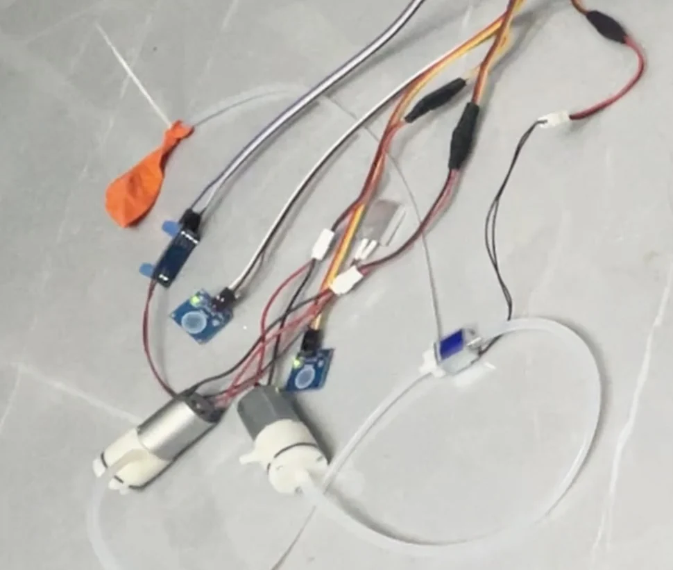 Air pumps, tubing, and electronics assembled on a worktable for a mechanism test.