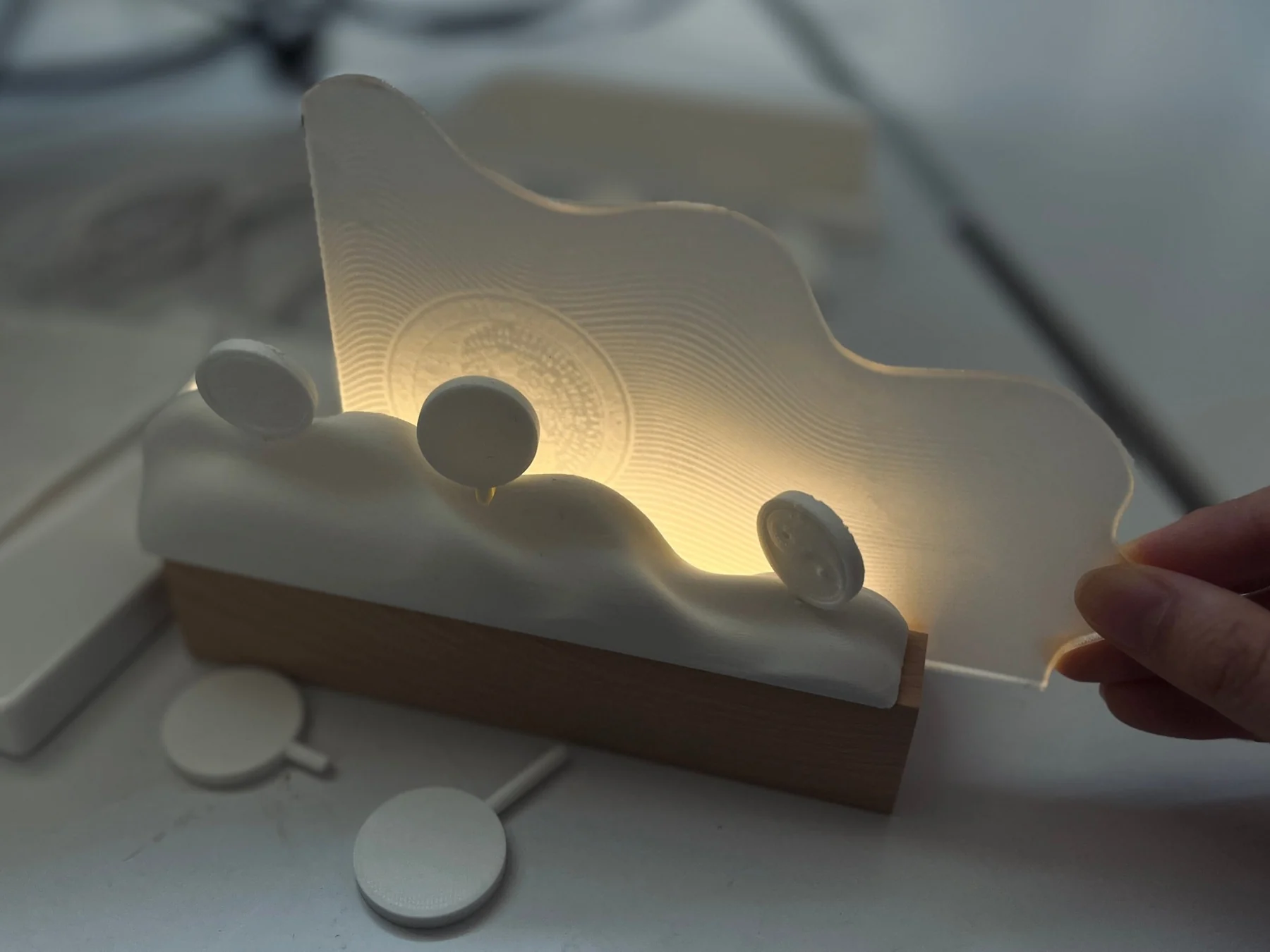A hand holds the assembled pale wave-like structure above its wooden base during a light test.