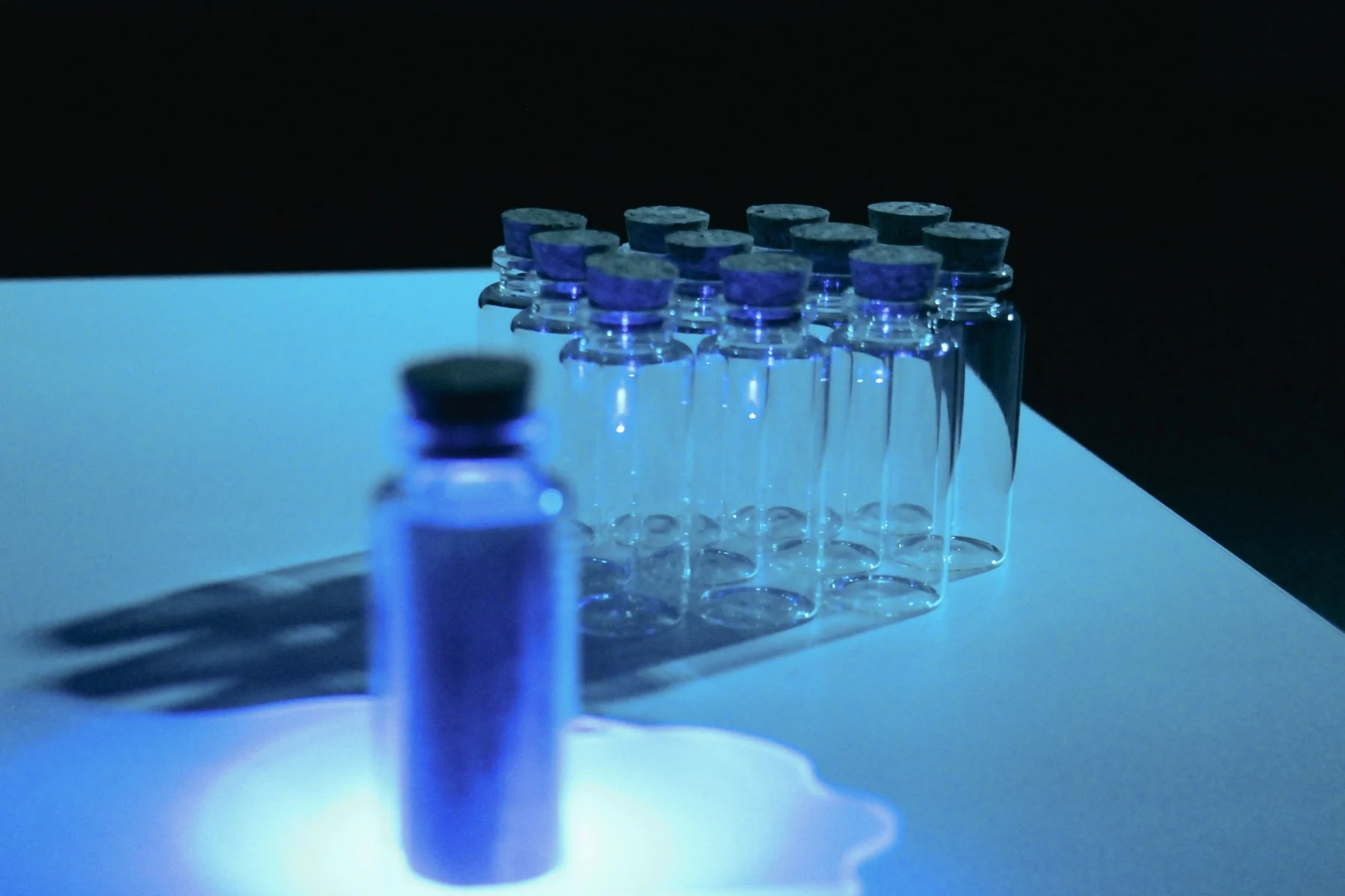Small glass bottles are arranged on a table in blue light, ready to hold printed readings.